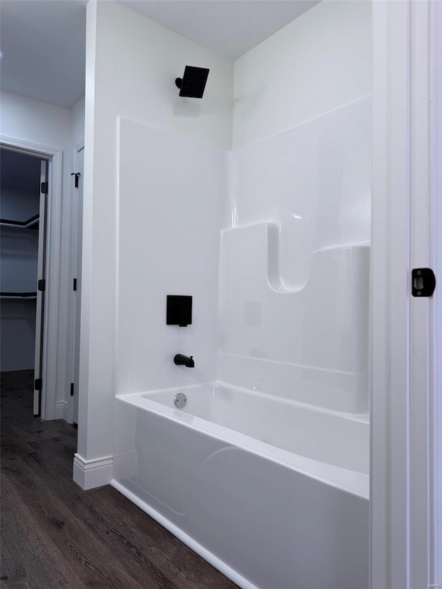 full bath with baseboards, a walk in closet, wood finished floors, and shower / bathing tub combination