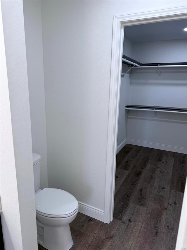 bathroom with baseboards, a spacious closet, toilet, and wood finished floors