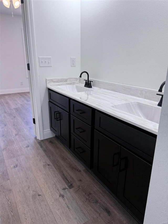 full bathroom featuring double vanity, wood finished floors, a sink, and baseboards