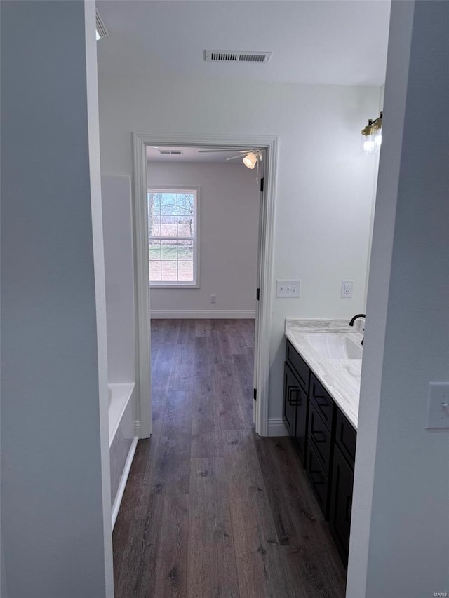 full bath featuring visible vents, a bathing tub, vanity, wood finished floors, and baseboards