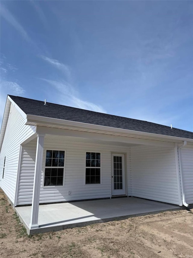 rear view of house featuring a shingled roof and a patio