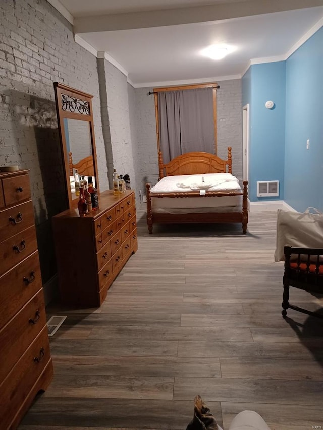 bedroom featuring hardwood / wood-style flooring, ornamental molding, and brick wall