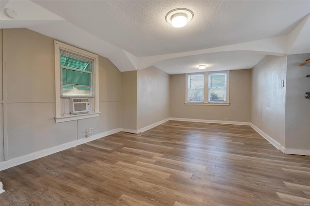 additional living space with lofted ceiling, cooling unit, wood-type flooring, and a textured ceiling