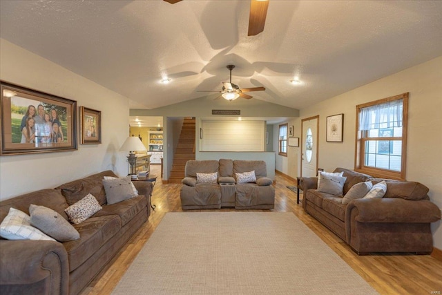 living room featuring ceiling fan, light wood-type flooring, a textured ceiling, and lofted ceiling