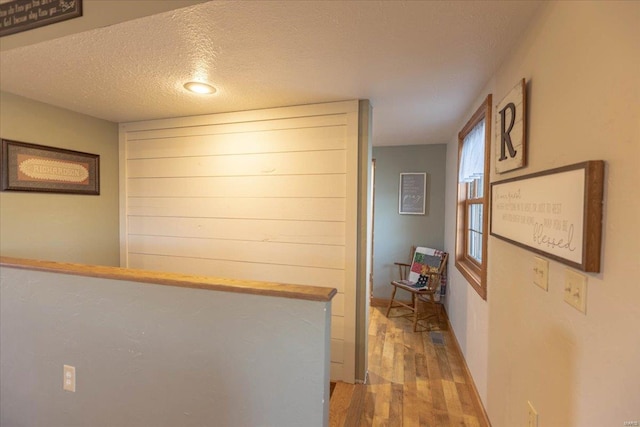 hall with light wood-type flooring and a textured ceiling