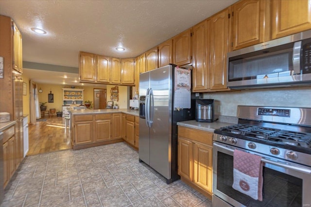 kitchen with a textured ceiling, appliances with stainless steel finishes, and kitchen peninsula