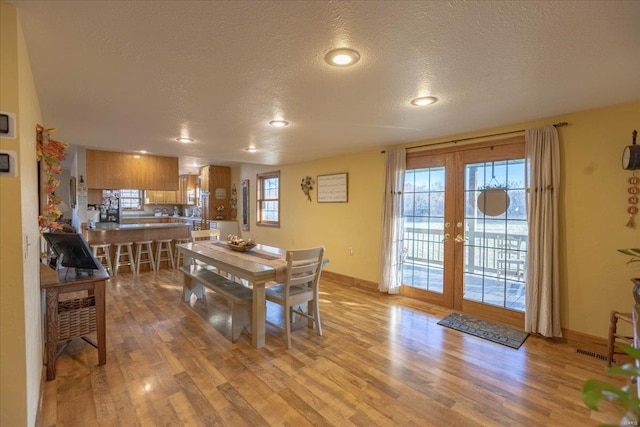 dining space with light hardwood / wood-style floors, a textured ceiling, and french doors