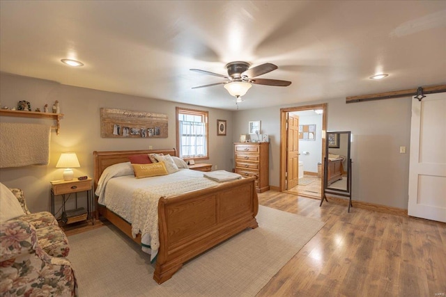 bedroom featuring ceiling fan, connected bathroom, a barn door, and light wood-type flooring