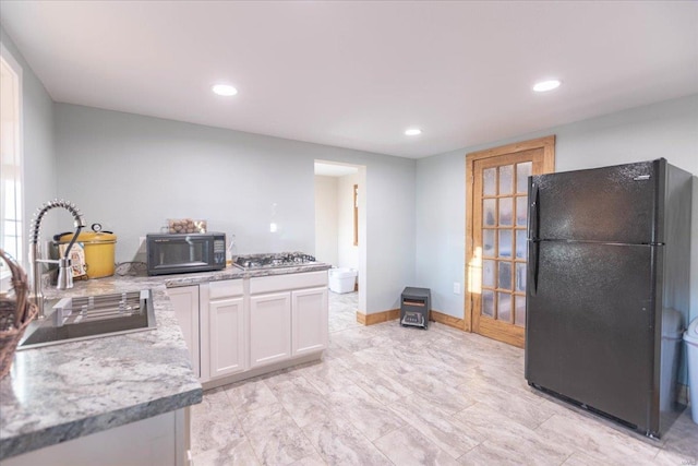 kitchen with black appliances, white cabinets, light stone countertops, and sink