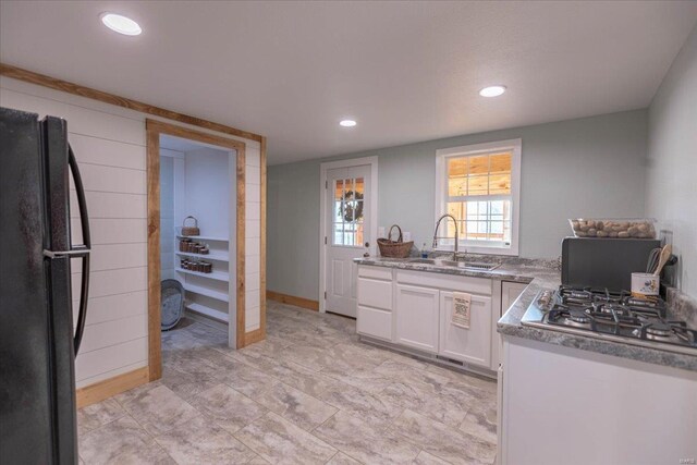 kitchen with sink, black fridge, stainless steel gas stovetop, and white cabinetry