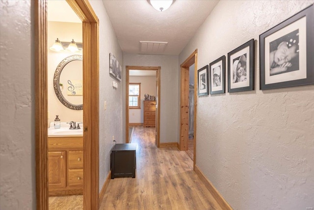 corridor with sink, a textured ceiling, and wood-type flooring