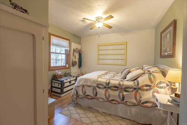 bedroom with ceiling fan, light hardwood / wood-style floors, and a textured ceiling