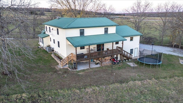 exterior space featuring a trampoline, central AC unit, a wooden deck, and a lawn