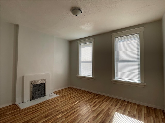 unfurnished living room featuring light hardwood / wood-style floors, a textured ceiling, a tile fireplace, and heating unit