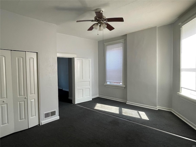 unfurnished bedroom featuring multiple windows, dark carpet, and ceiling fan