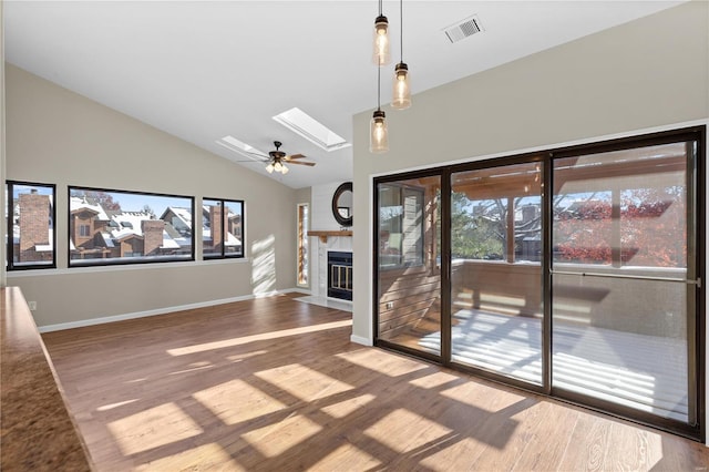 unfurnished living room with hardwood / wood-style flooring, a large fireplace, high vaulted ceiling, and a skylight