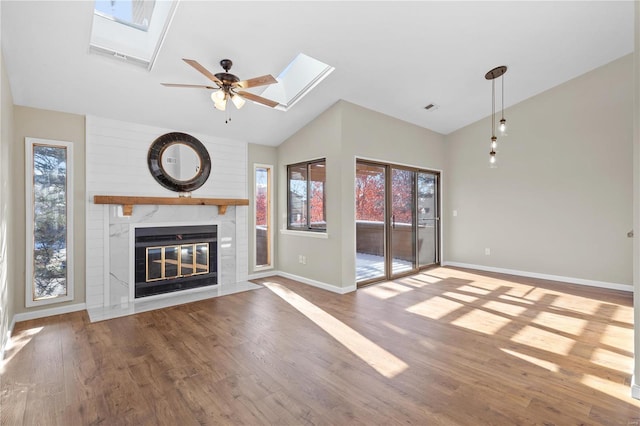 unfurnished living room with ceiling fan, a fireplace, vaulted ceiling with skylight, and hardwood / wood-style floors