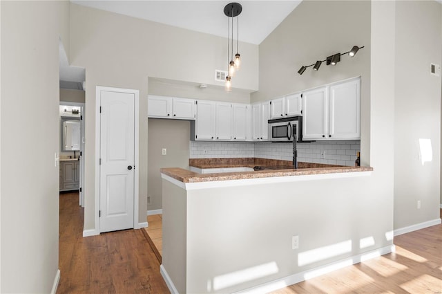 kitchen with decorative light fixtures, kitchen peninsula, a towering ceiling, decorative backsplash, and white cabinets