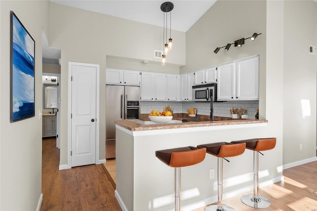 kitchen with a towering ceiling, tasteful backsplash, white cabinets, kitchen peninsula, and stainless steel appliances