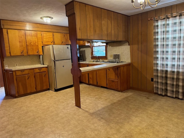 kitchen with wood walls, sink, decorative backsplash, a notable chandelier, and white fridge