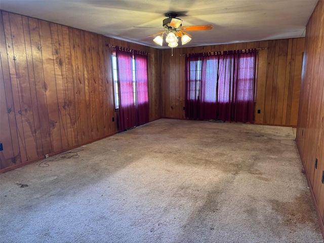 carpeted spare room with wood walls and ceiling fan