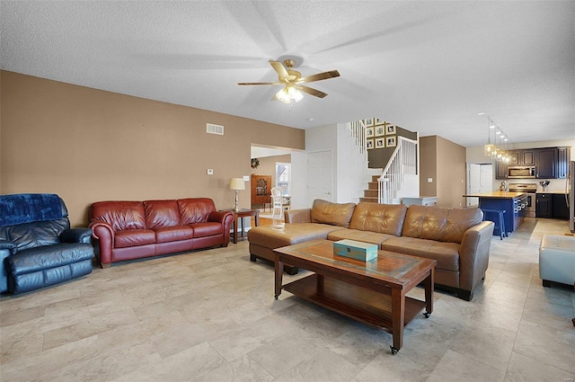 living room featuring ceiling fan with notable chandelier and a textured ceiling