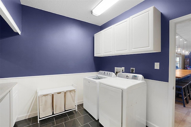 clothes washing area featuring dark tile patterned flooring, cabinets, a textured ceiling, and washing machine and dryer