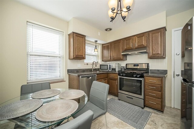 kitchen featuring sink, stainless steel appliances, a notable chandelier, decorative light fixtures, and decorative backsplash