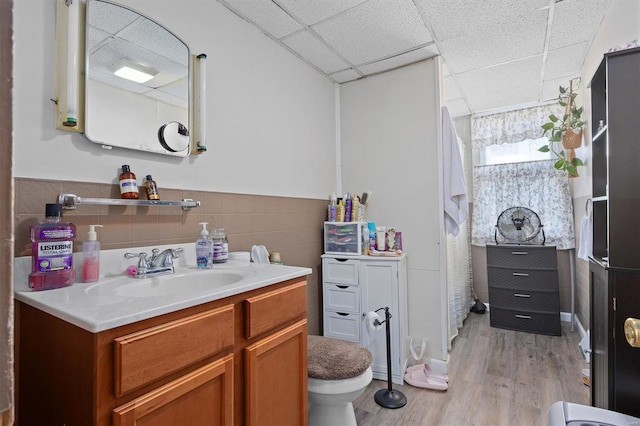 bathroom featuring hardwood / wood-style floors, a drop ceiling, vanity, toilet, and tile walls