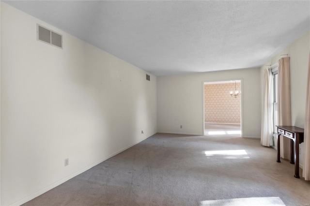 spare room with light colored carpet and an inviting chandelier