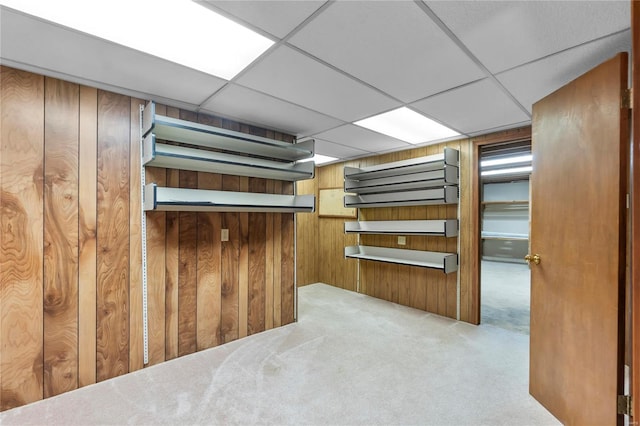 basement featuring a paneled ceiling, light colored carpet, and wooden walls