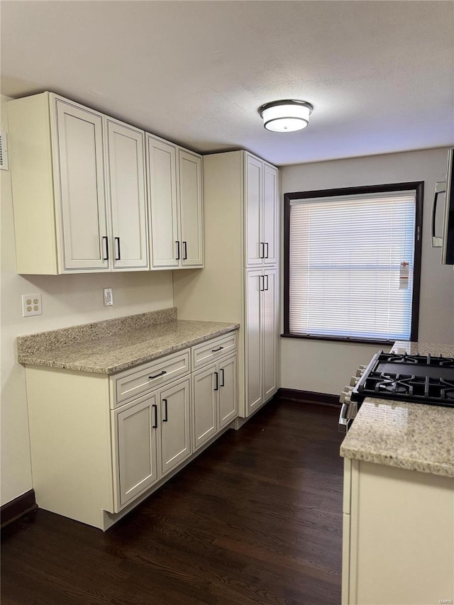 kitchen with white cabinets, light stone counters, stainless steel range with gas cooktop, and dark wood-type flooring