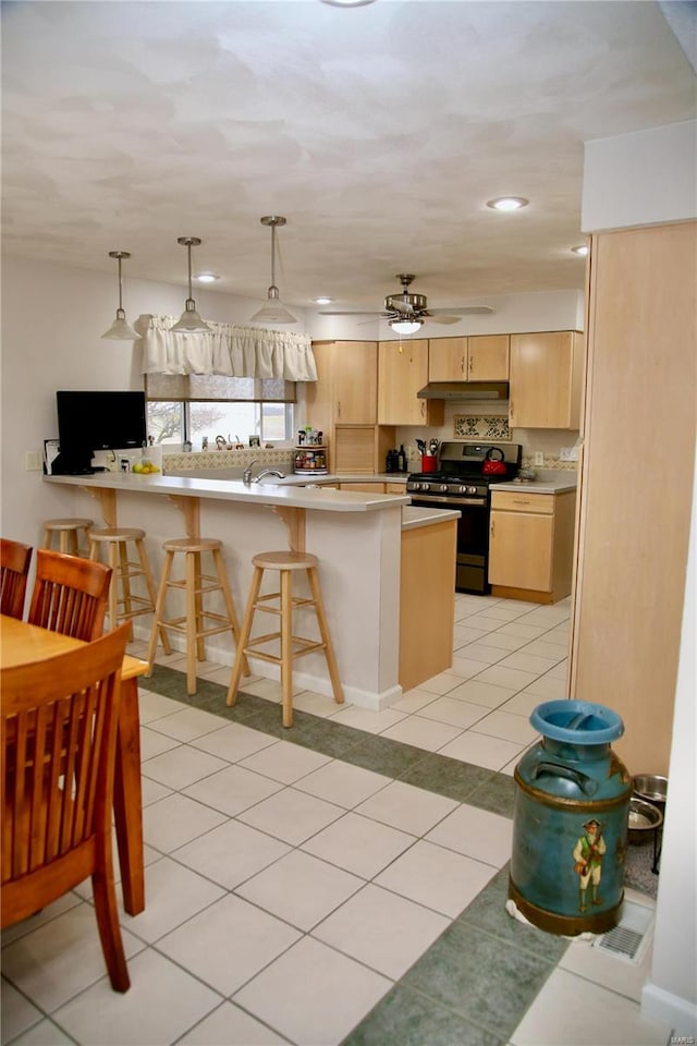 kitchen with kitchen peninsula, light brown cabinetry, a kitchen bar, ceiling fan, and stainless steel range with gas stovetop