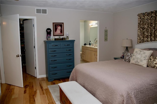 bedroom with a spacious closet, sink, connected bathroom, and light hardwood / wood-style flooring