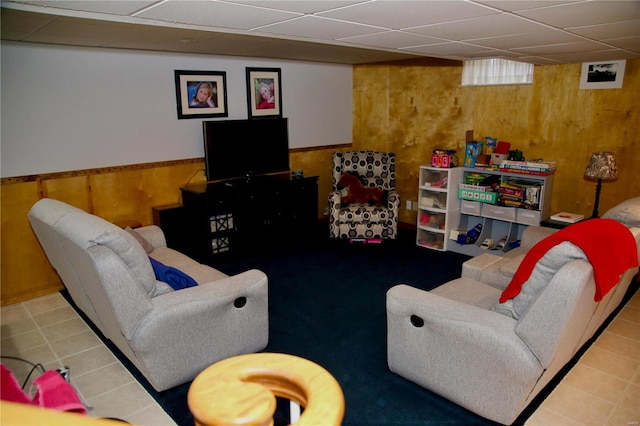 living room with tile patterned floors, a paneled ceiling, and wood walls