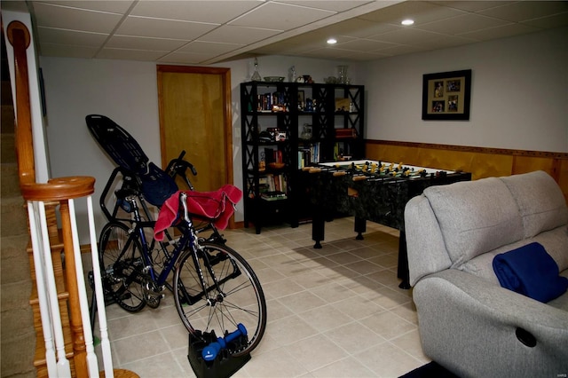 rec room with a paneled ceiling, wood walls, and light tile patterned flooring