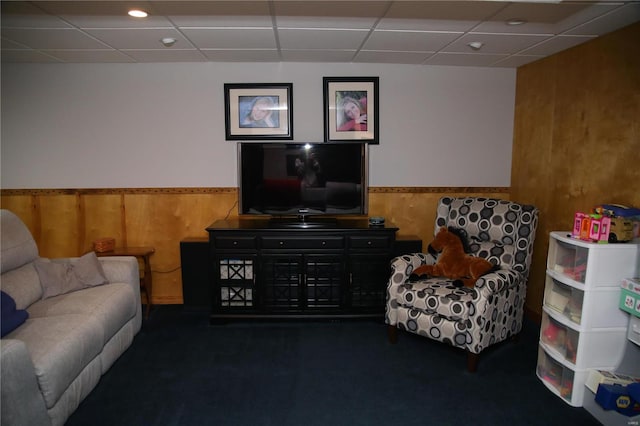 living area with a drop ceiling and wood walls