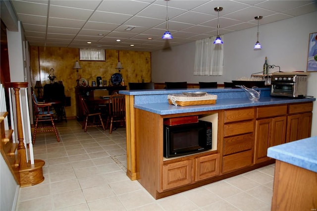 kitchen featuring a paneled ceiling, decorative light fixtures, wood walls, and light tile patterned flooring