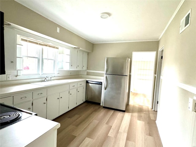 kitchen with sink, decorative backsplash, light wood-type flooring, appliances with stainless steel finishes, and white cabinetry