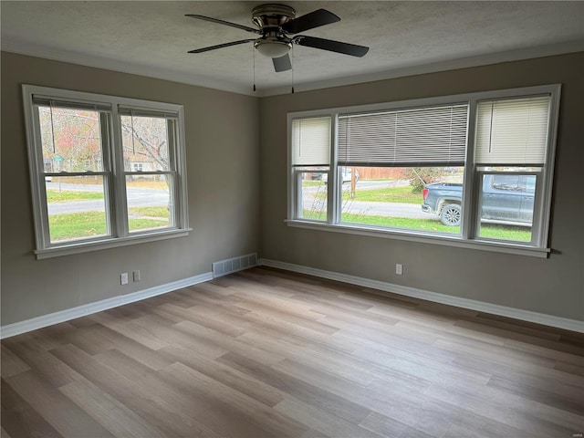 empty room featuring ceiling fan, light hardwood / wood-style flooring, a textured ceiling, and ornamental molding