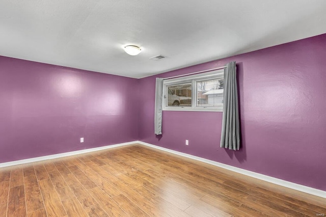 empty room with wood finished floors, visible vents, and baseboards