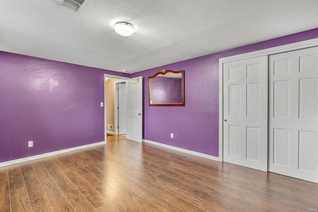 unfurnished bedroom featuring a closet, wood finished floors, visible vents, and baseboards