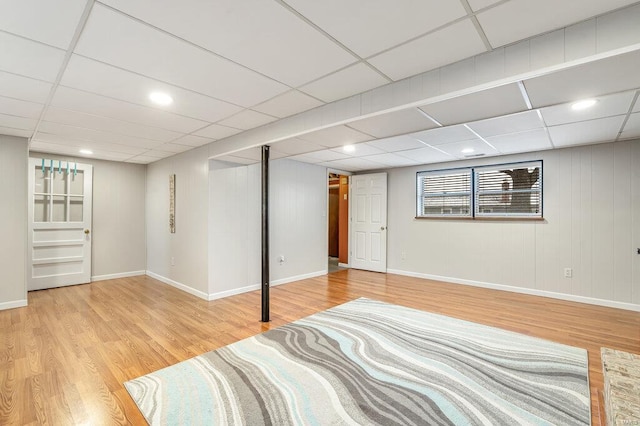 below grade area with a paneled ceiling, baseboards, and wood finished floors