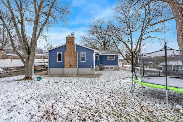 snow covered house featuring a trampoline, a chimney, and fence