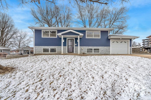 raised ranch featuring a garage, stone siding, and fence