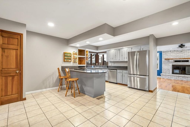 kitchen with light tile patterned floors, baseboards, dark countertops, appliances with stainless steel finishes, and a peninsula