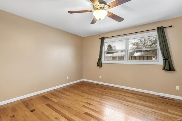 empty room with a ceiling fan, visible vents, light wood finished floors, and baseboards