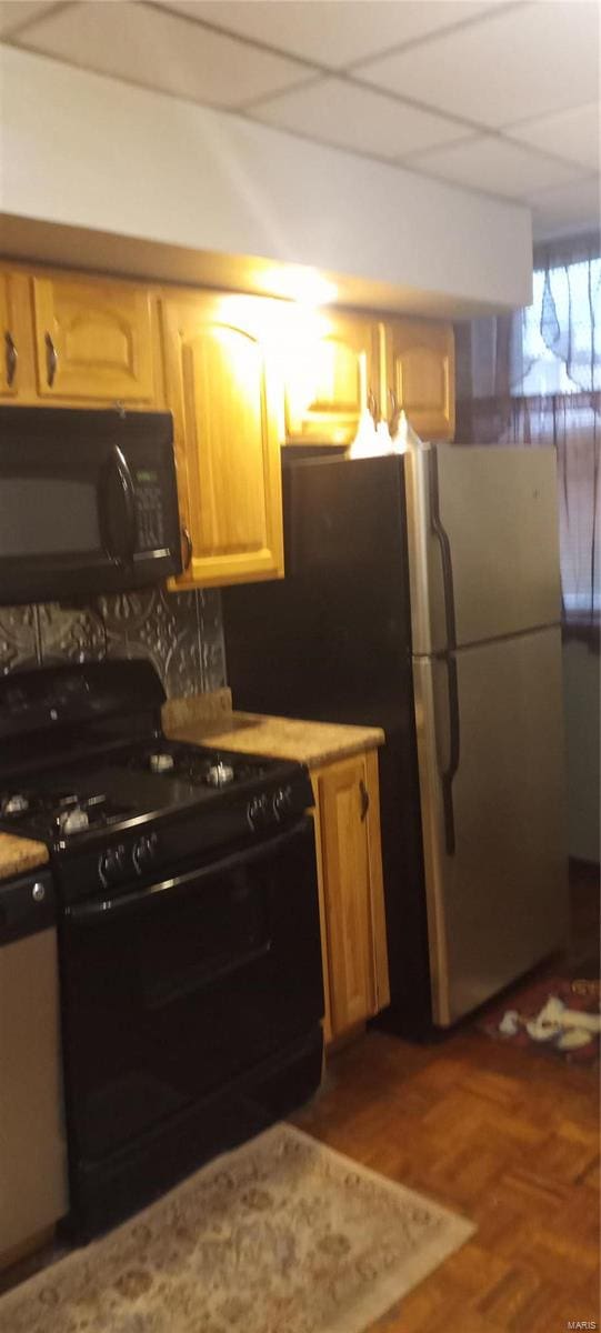 kitchen featuring a drop ceiling, black appliances, and light brown cabinets