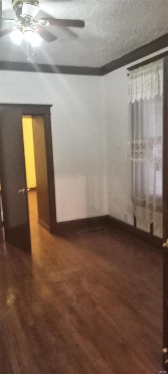 spare room with a textured ceiling, ceiling fan, and dark wood-type flooring