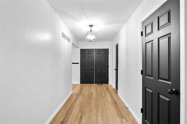 hall featuring light wood-type flooring and a notable chandelier